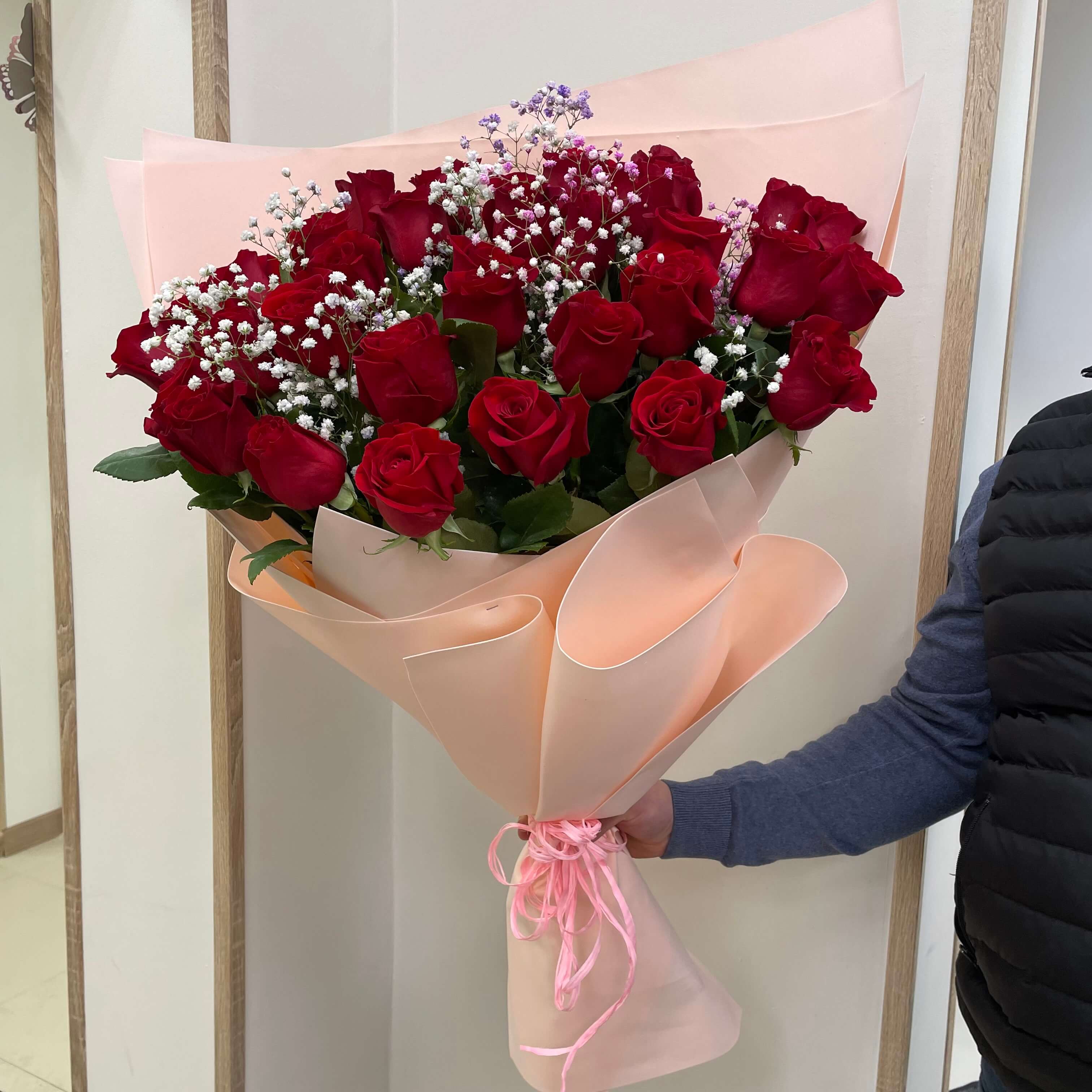 Stunning arrangement of deep red roses with baby's breath, elegantly presented in peach wrapping.