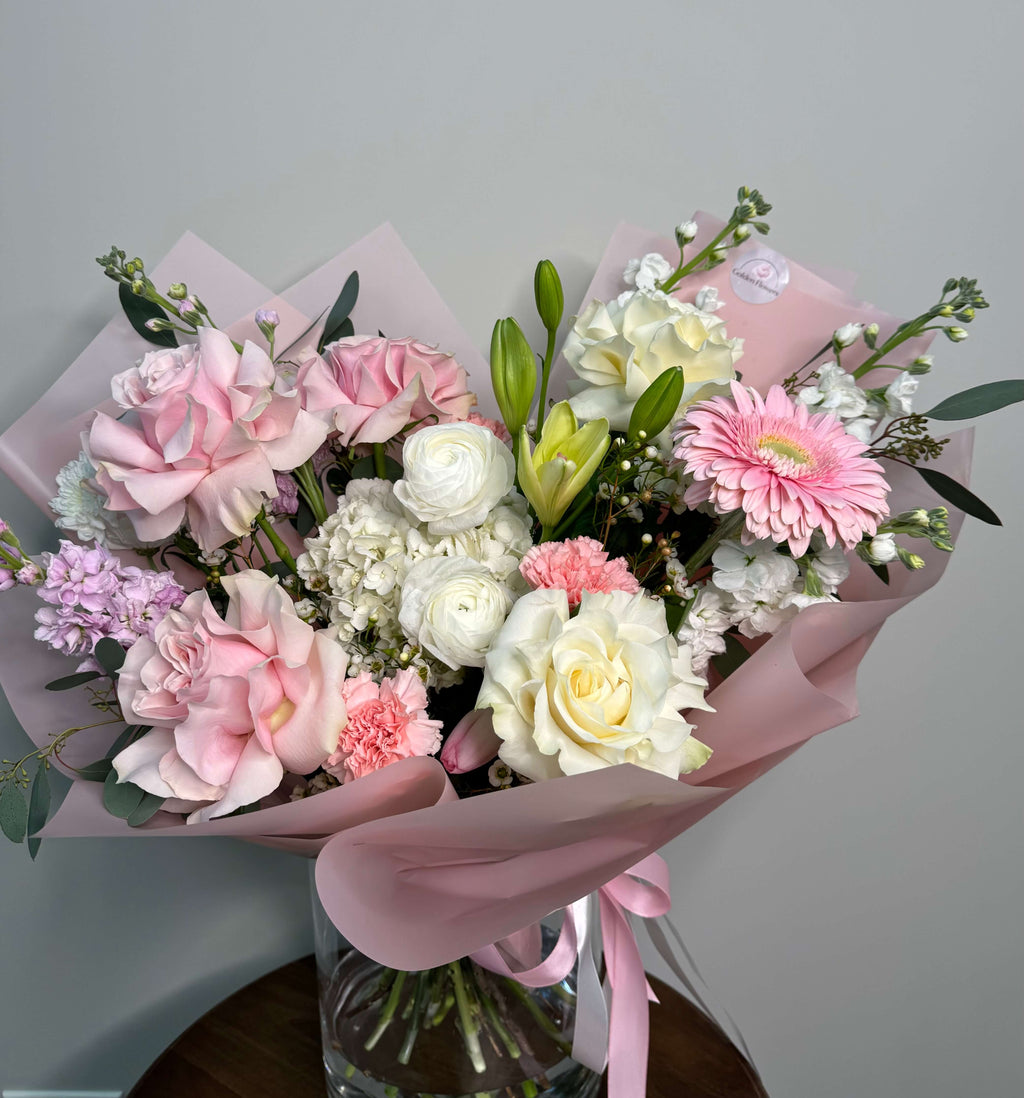 Delicate floral composition with pink and white roses, gerbera daisies, and soft greenery.