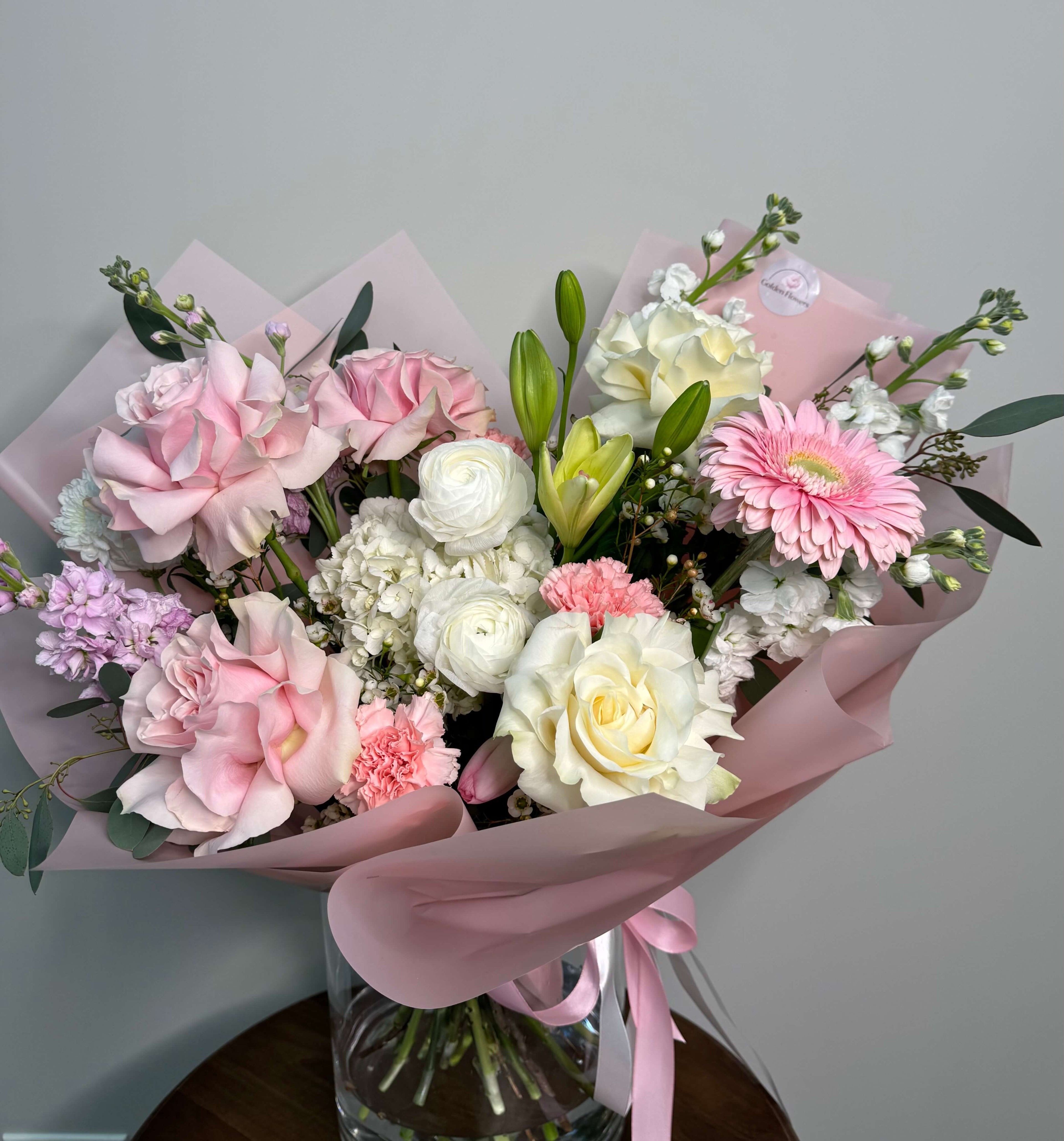 Delicate floral composition with pink and white roses, gerbera daisies, and soft greenery.