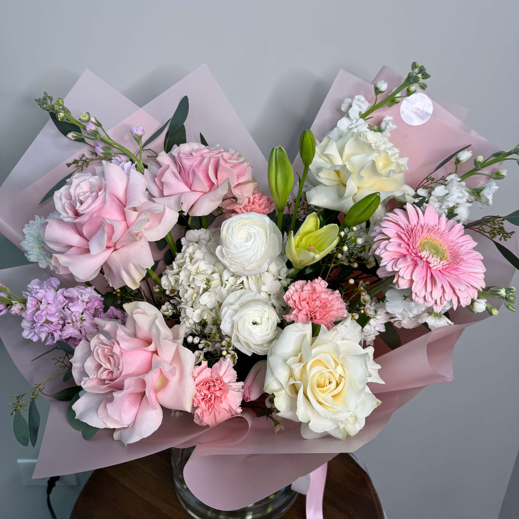 An elegant arrangement of white orchids and pale pink roses, beautifully complemented by baby's breath and lush foliage.