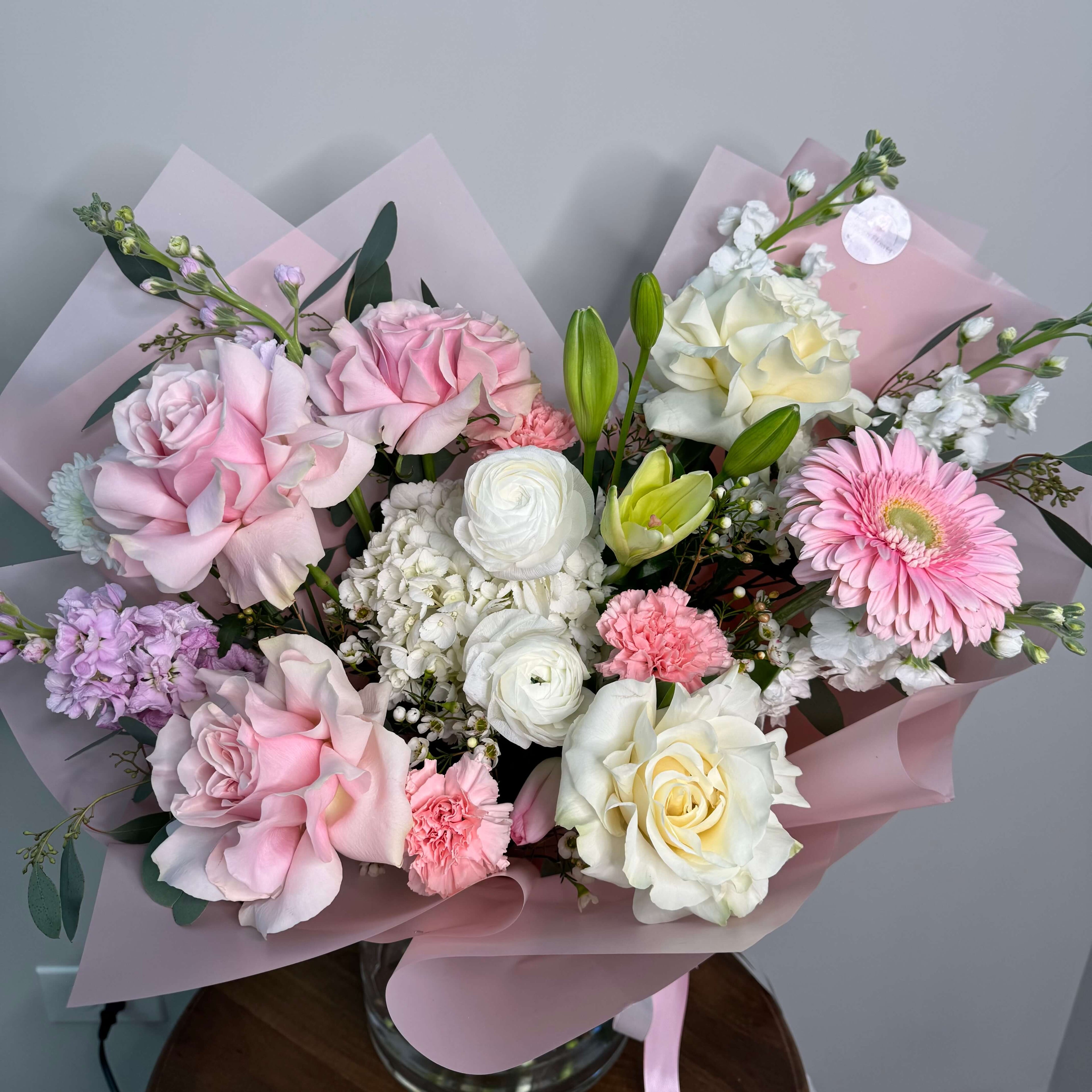 An elegant arrangement of white orchids and pale pink roses, beautifully complemented by baby's breath and lush foliage.
