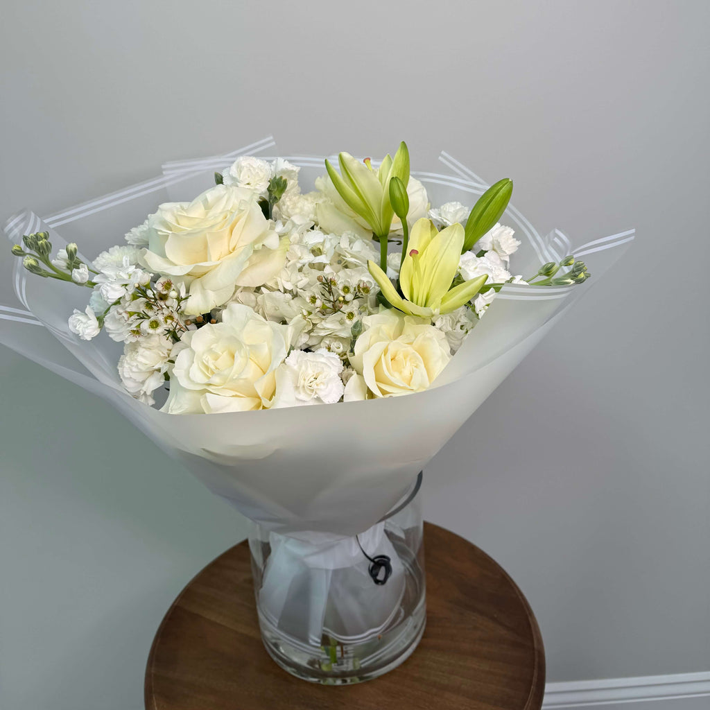A vibrant and lively bouquet with white and peach roses, delicately arranged in deep burgundy wrapping.