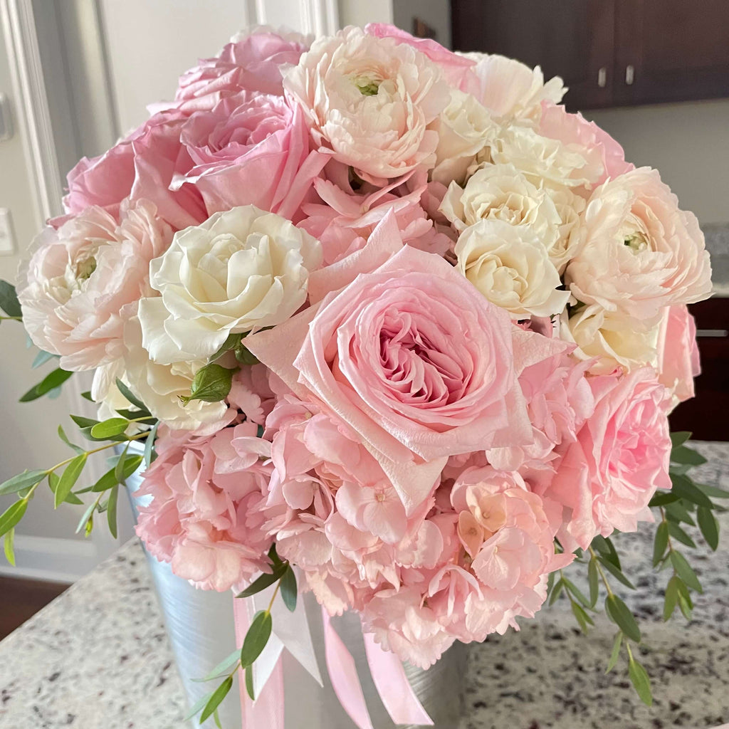 A pastel floral arrangement with pink roses, white carnations, and hydrangeas, delicately placed in a round box.