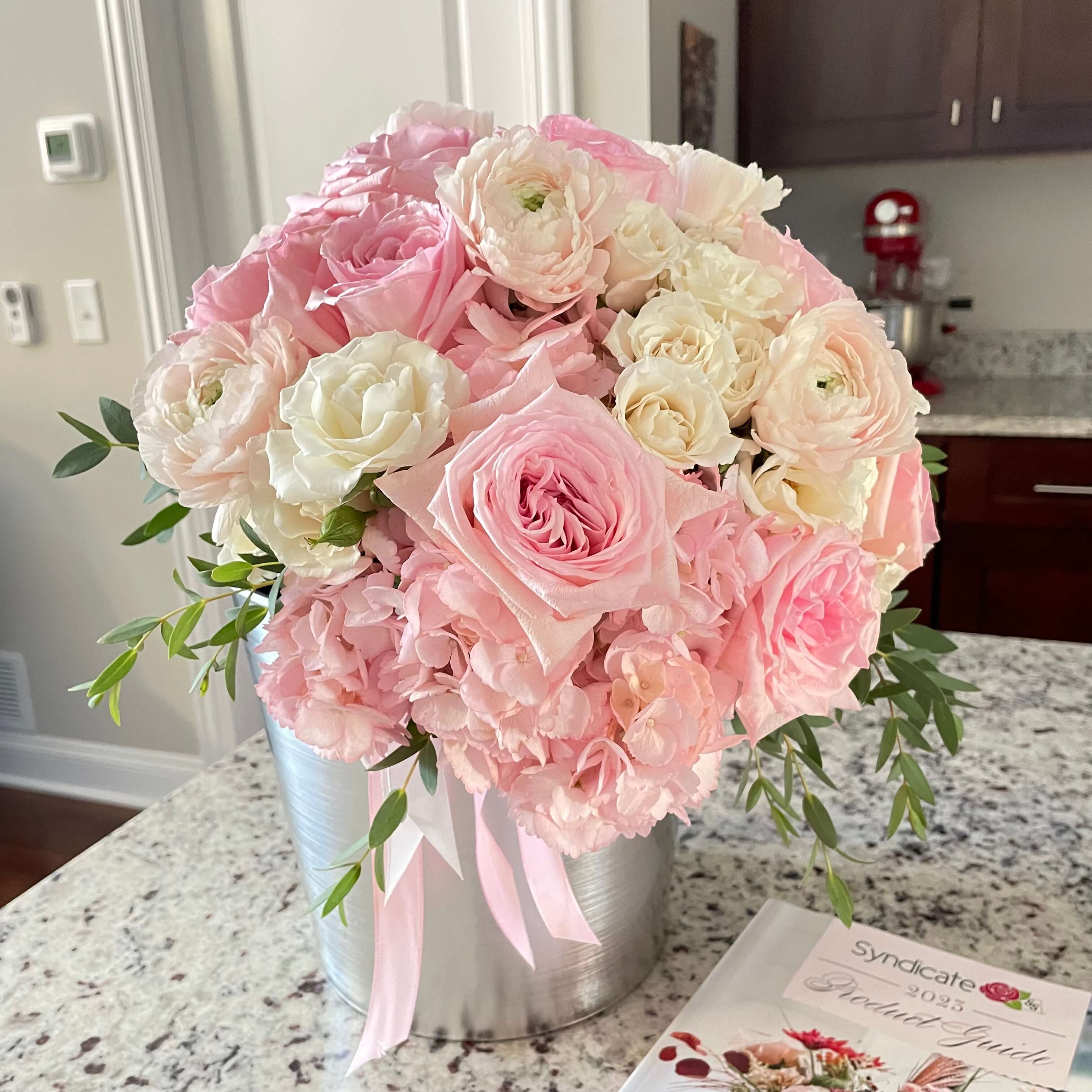 A luxurious floral arrangement with pink and white roses, hydrangeas, and delicate details in a stylish silver container.