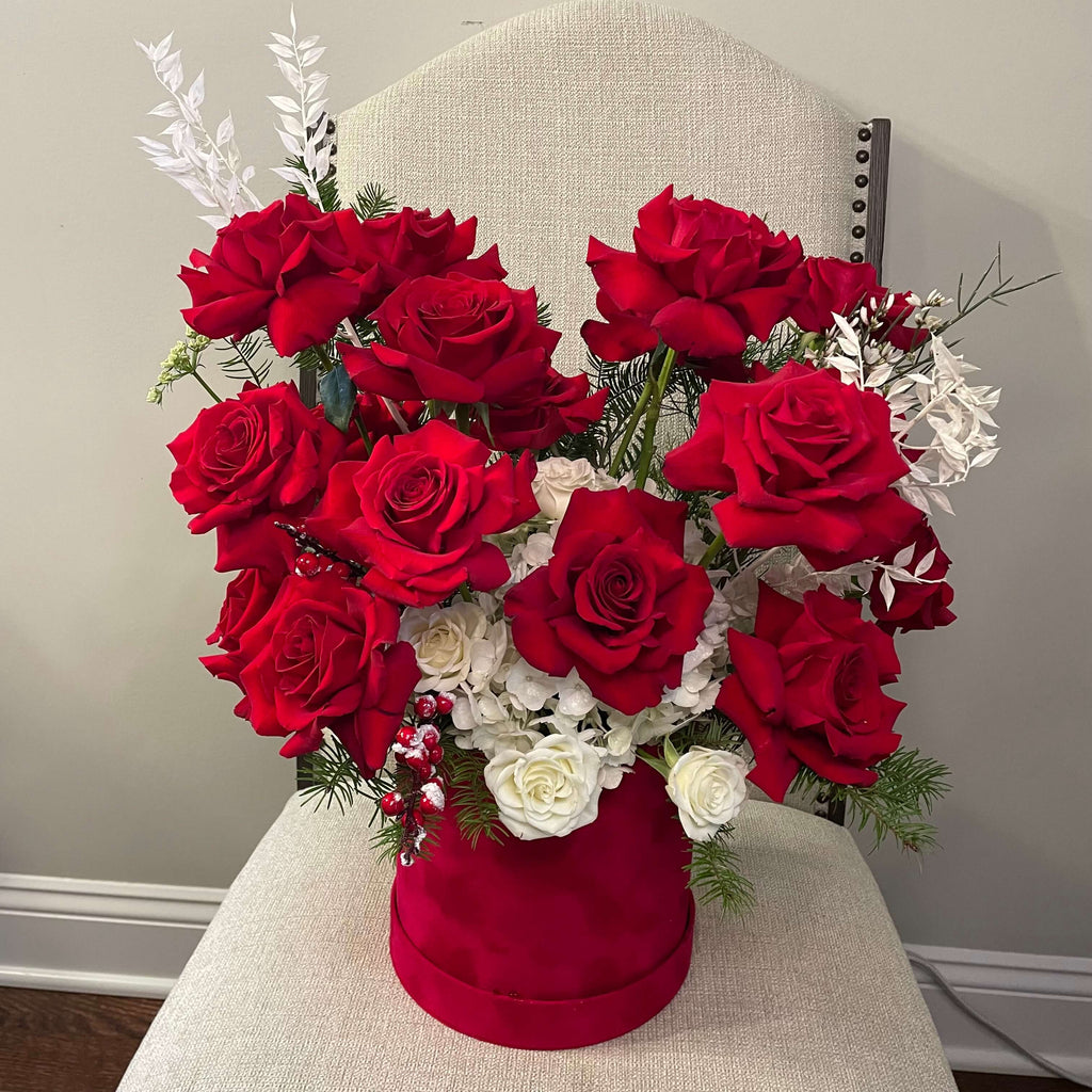 A pastel-themed bouquet with blush white hydrangeas, white lilies, and red roses wrapped in delicate red boxes.