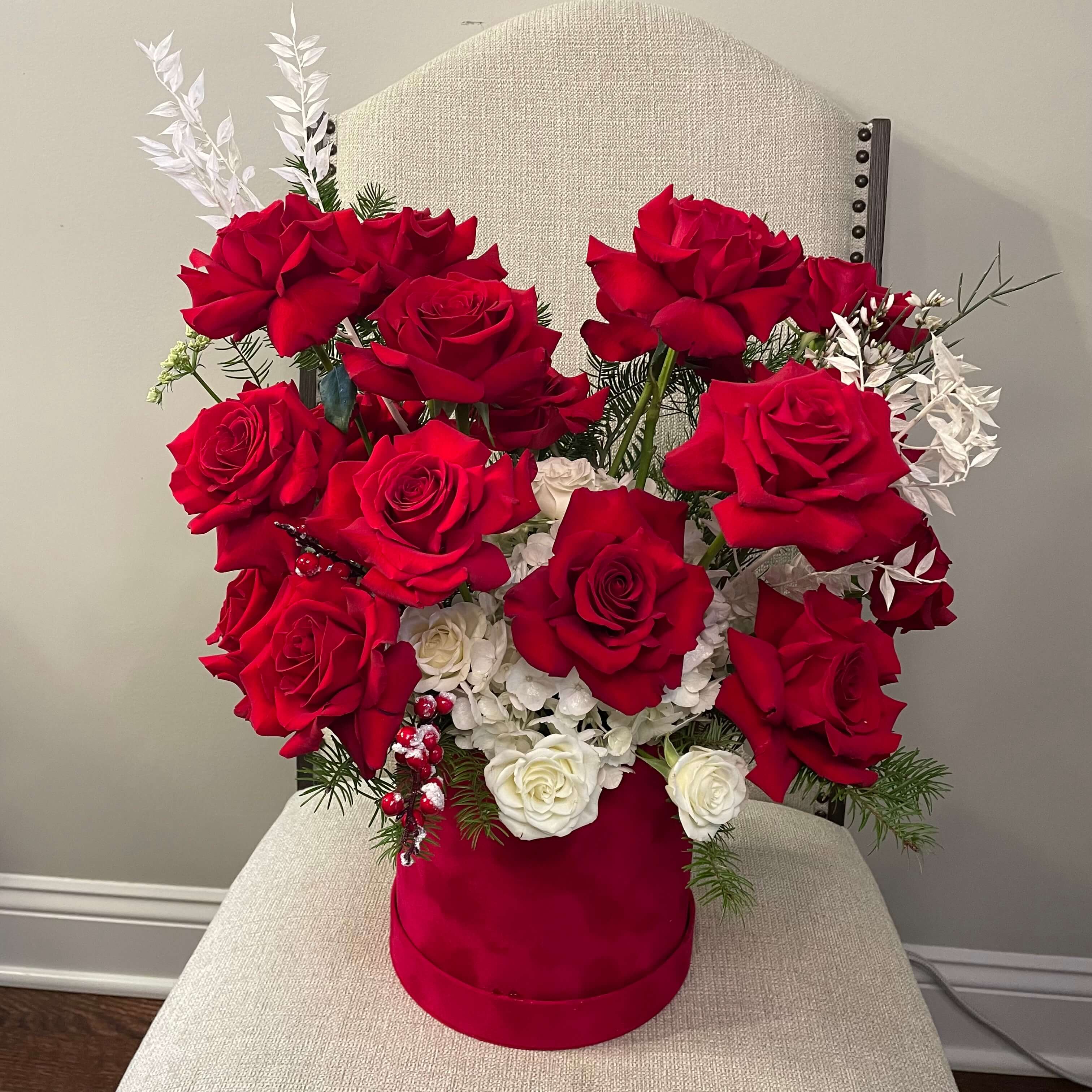 A pastel-themed bouquet with blush white hydrangeas, white lilies, and red roses wrapped in delicate red boxes.